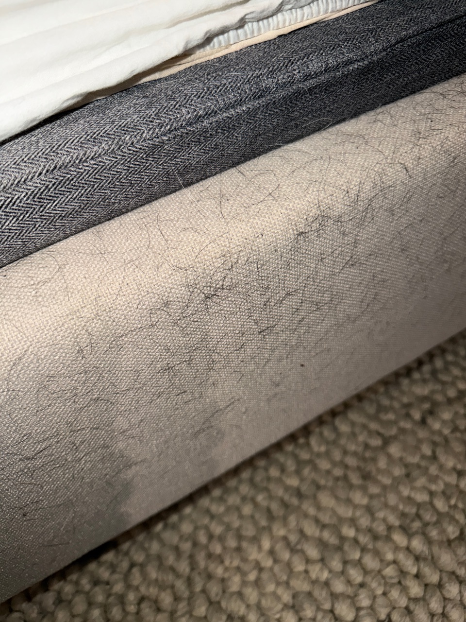 Upholstered bed frame before cleaning: the fabric is covered in hair and lint.